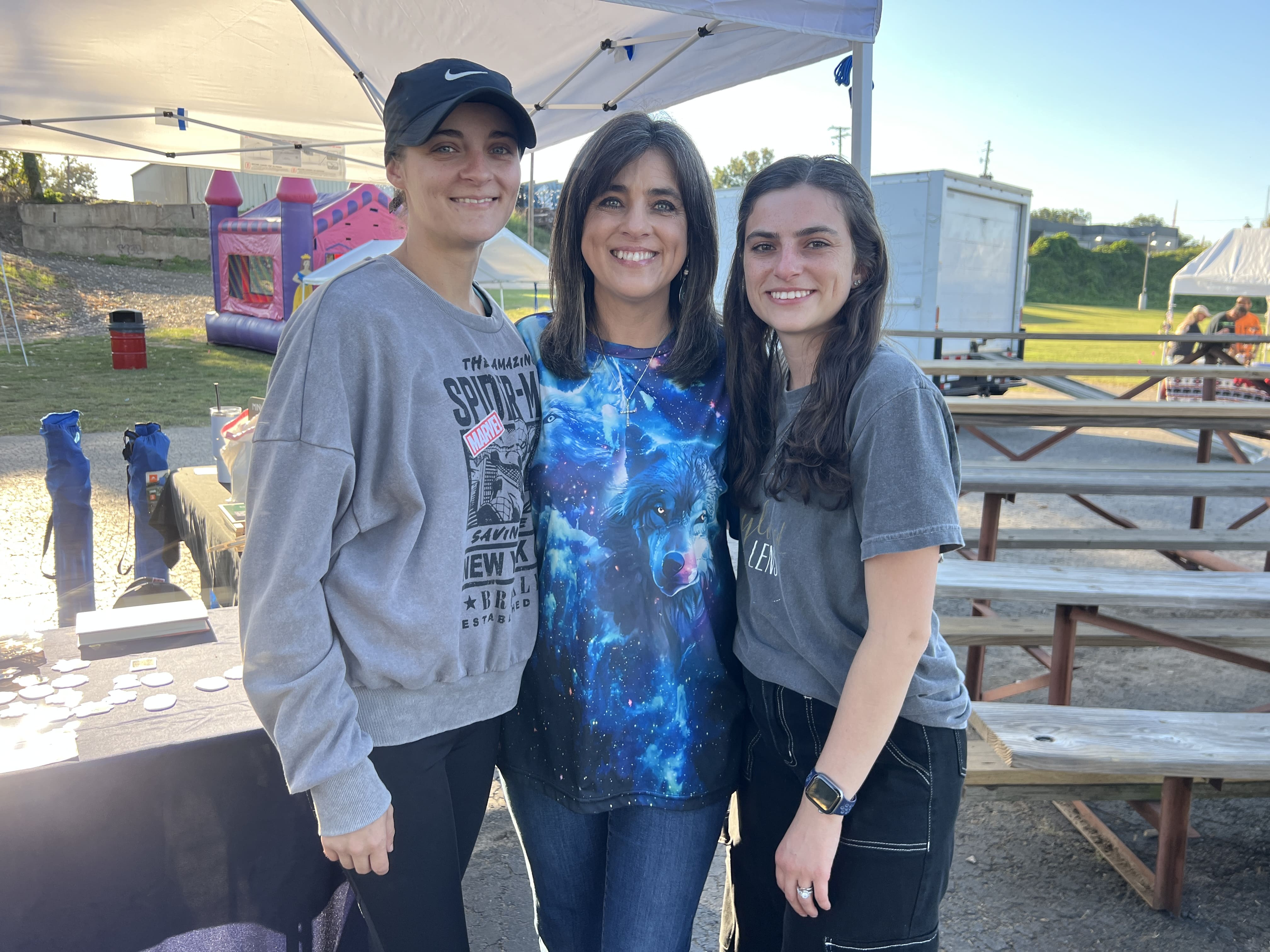 Three women smiling together at a vendor booth at October Festival 2025
